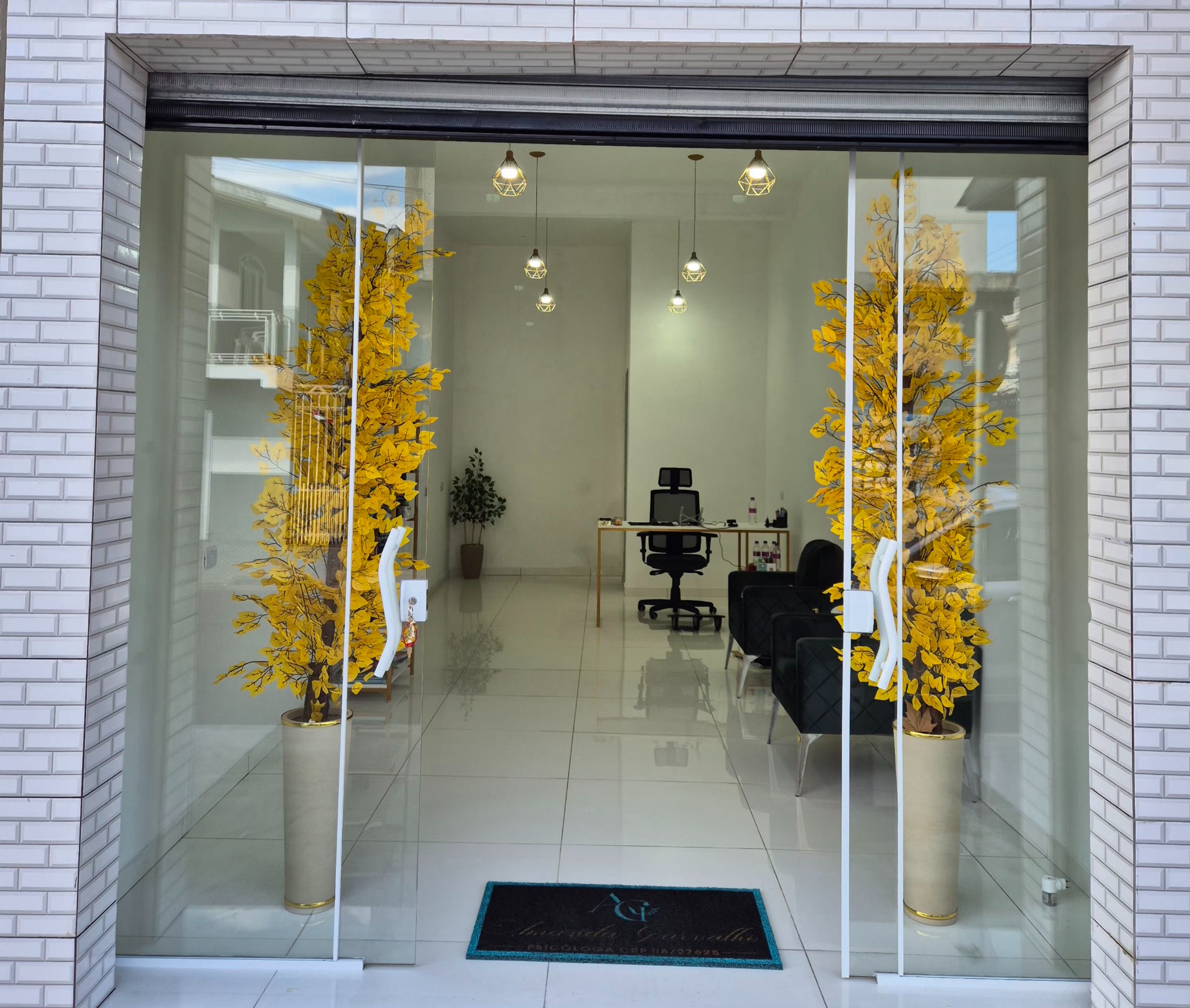 Entrada do espaço profissional de Amanda Carvalho, com portas de vidro e árvores decorativas amarelas